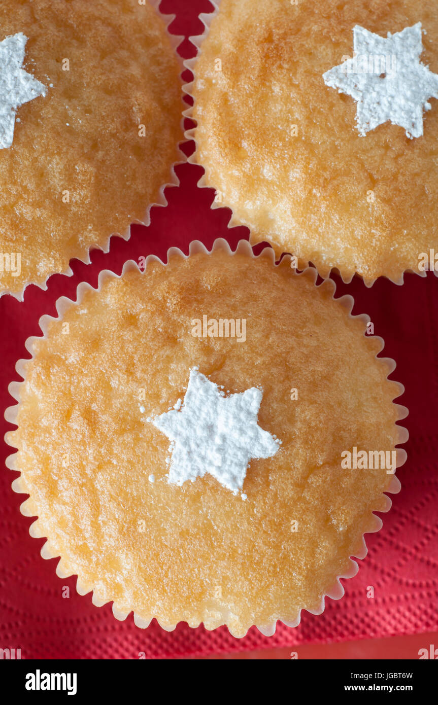 Overhead Schuss drei Vanille Cupcakes in Papier Fällen auf rotem Papierserviette, dekoriert mit bestreut weißen Puderzucker in Form von Sternen. Stockfoto