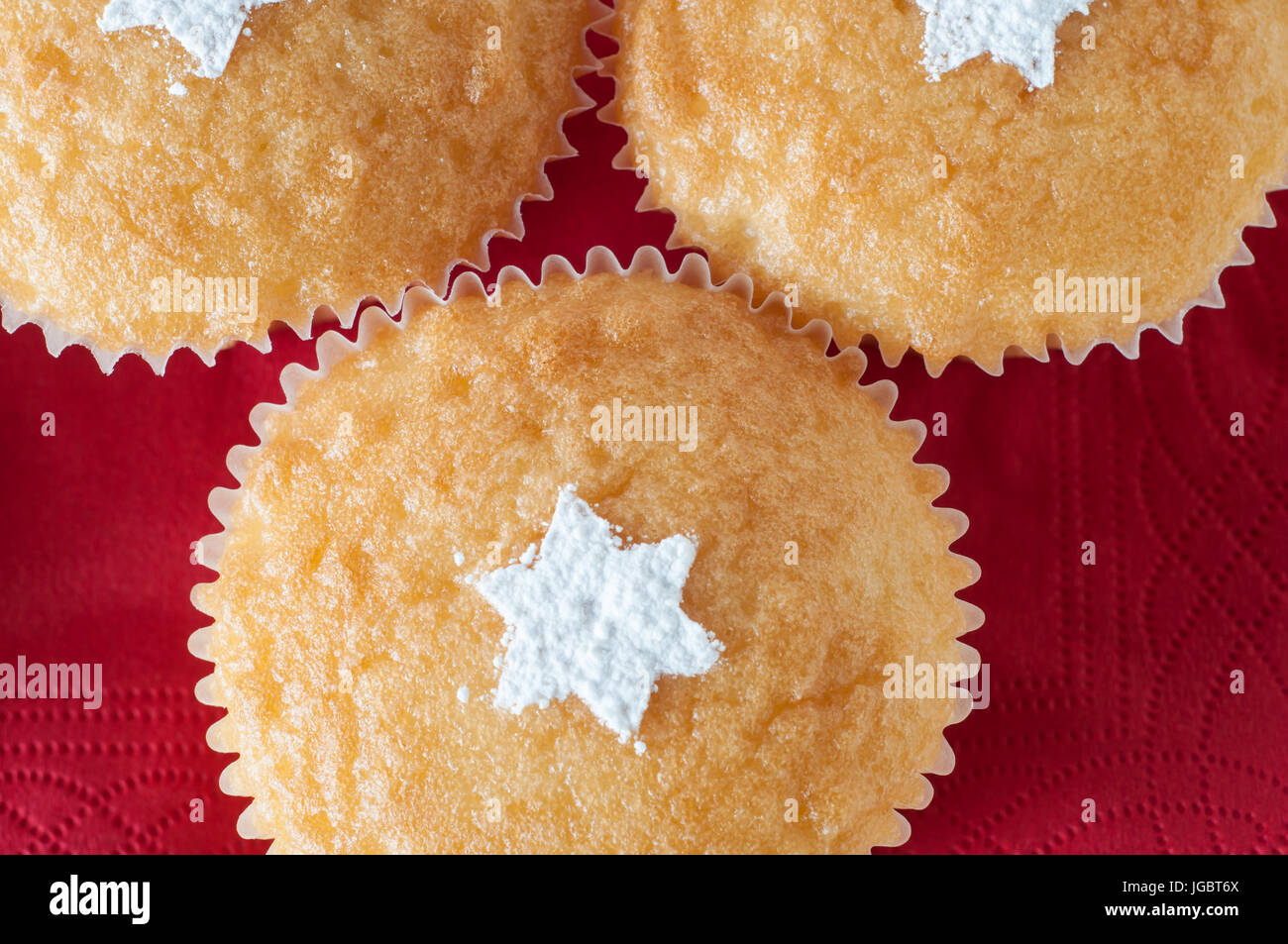 Drei Vanille Cupcakes auf einer roten Serviette Hintergrund, weit in die Höhe geschnellt und Gemeinkosten, dekoriert für Weihnachten mit Sternformen in weiß Puderzucker bestreut Stockfoto