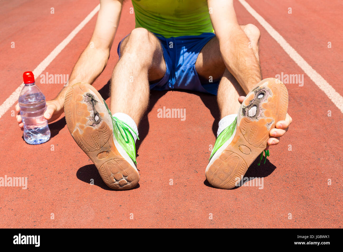 Athlet erschöpft auf einer Laufstrecke gebrochene grüne Laufschuhe mit großen Löchern in der Sohle tragen. Stockfoto