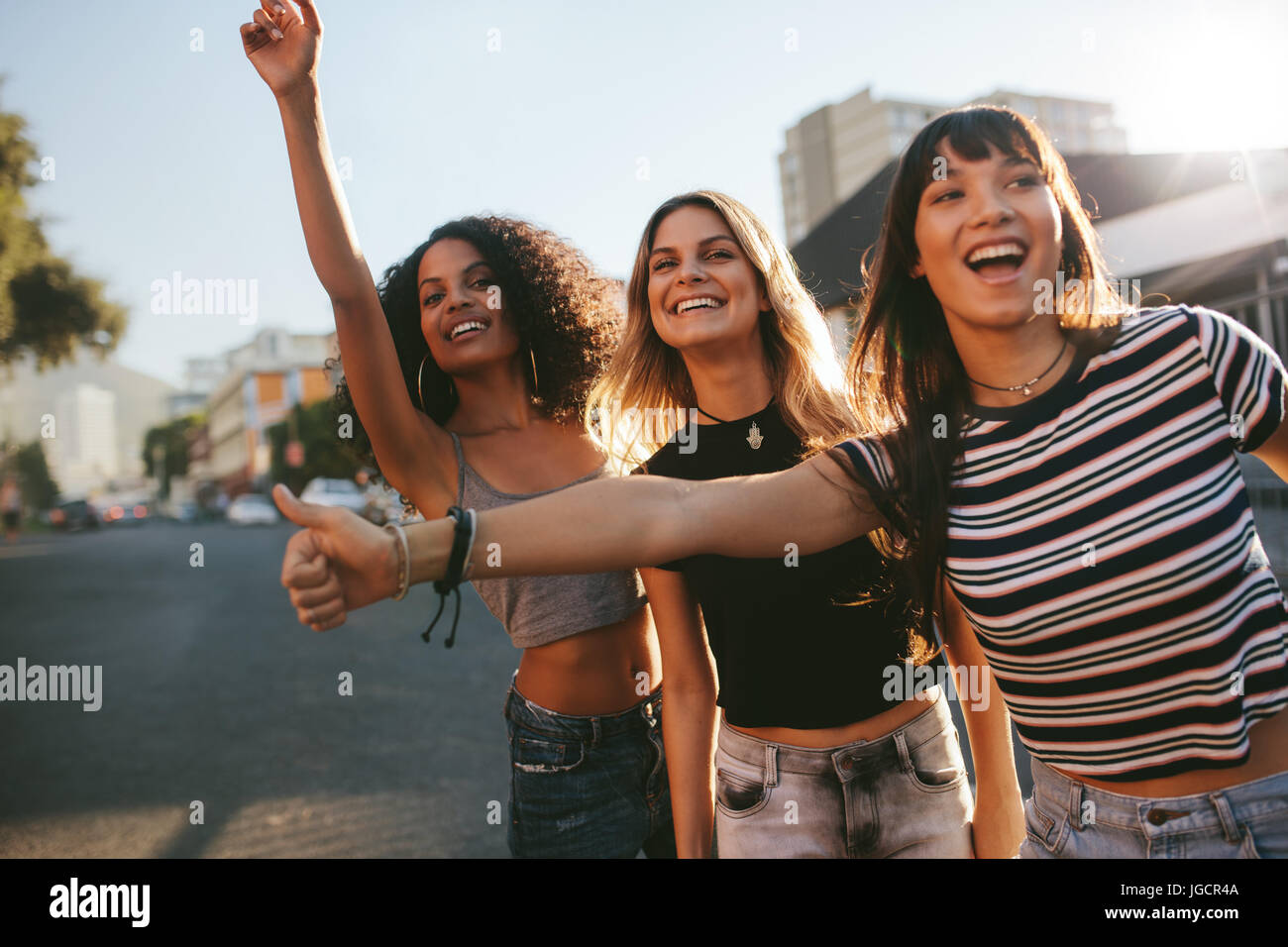 Drei junge Frauen stehen im Freien und ein Taxi rufen. Freundinnen warten auf eine Fahrt, für ein Taxi auf Stadtstraße gestikulieren. Stockfoto