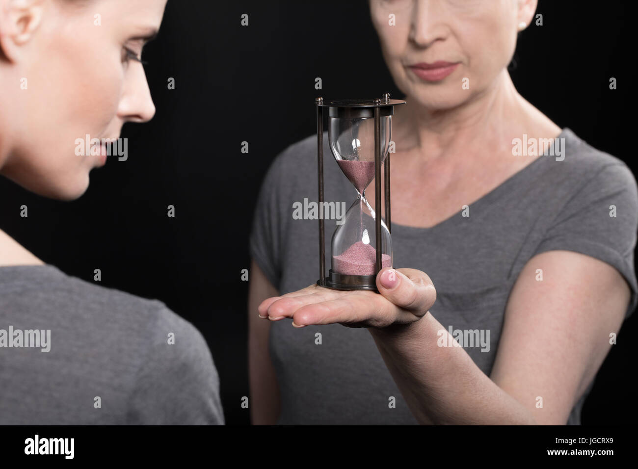 ältere Frau mit Sanduhr an seine Tochter isoliert auf schwarz Stockfoto