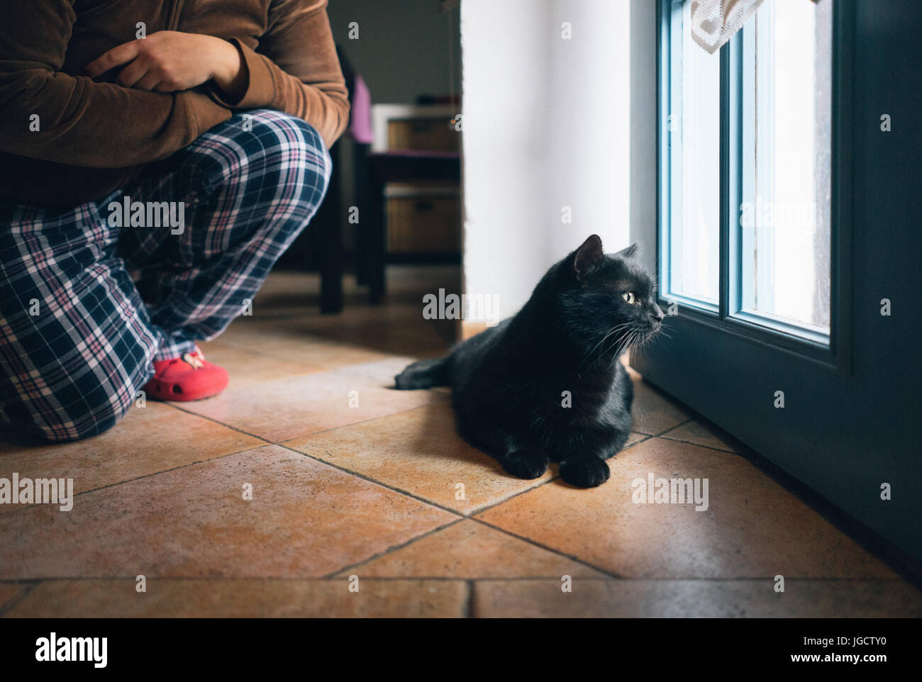 Frau kniete von ihrer Katze, die aus der Tür sucht Stockfoto