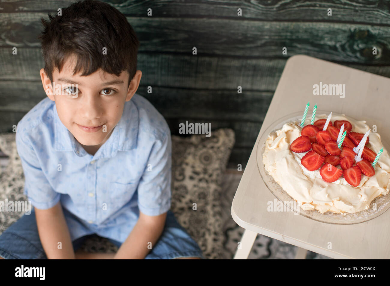 Junge sitzt neben einem Geburtstagskuchen Stockfoto