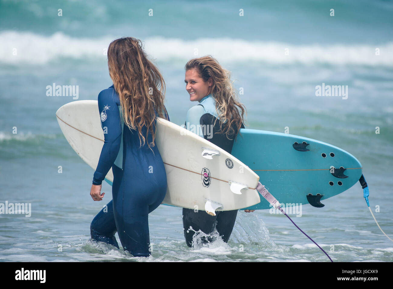 Surfen-UK; Zwei weibliche Surfer tragen ihre Surfbretter, als sie am Fistral in Newquay, Cornwall ins Meer gehen. Stockfoto