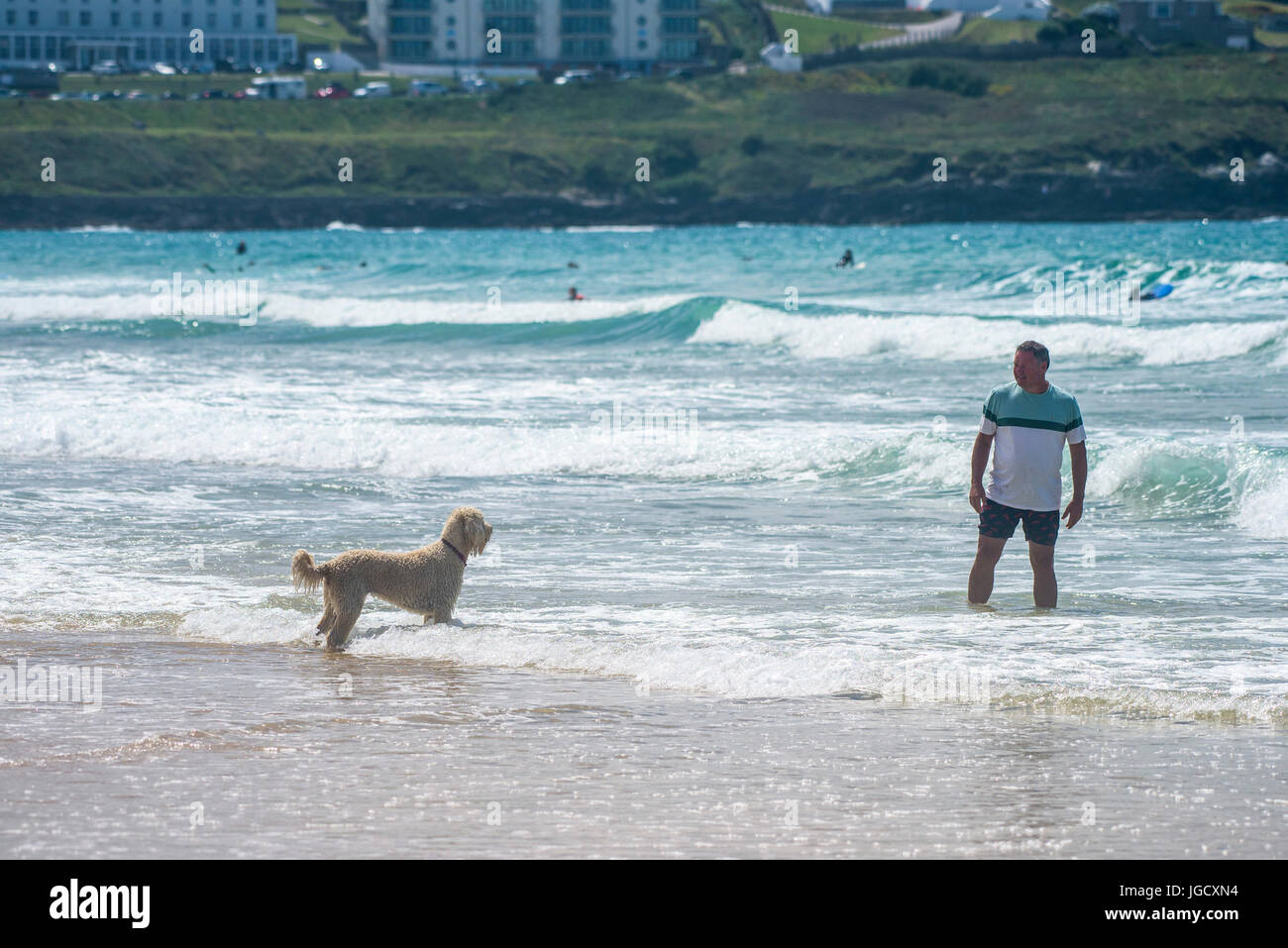Menschen am Strand. Ein Urlauber spielen mit seinem Hund in das Meer am Fistral Beach in Newquay, Cornwall. Stockfoto