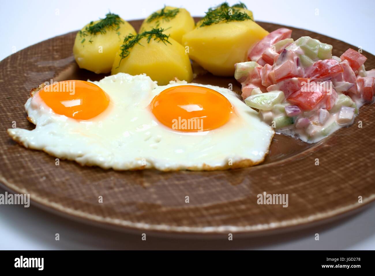 Spiegelei mit frischen Kartoffeln und Tomaten-Gurken-Salat. Stockfoto