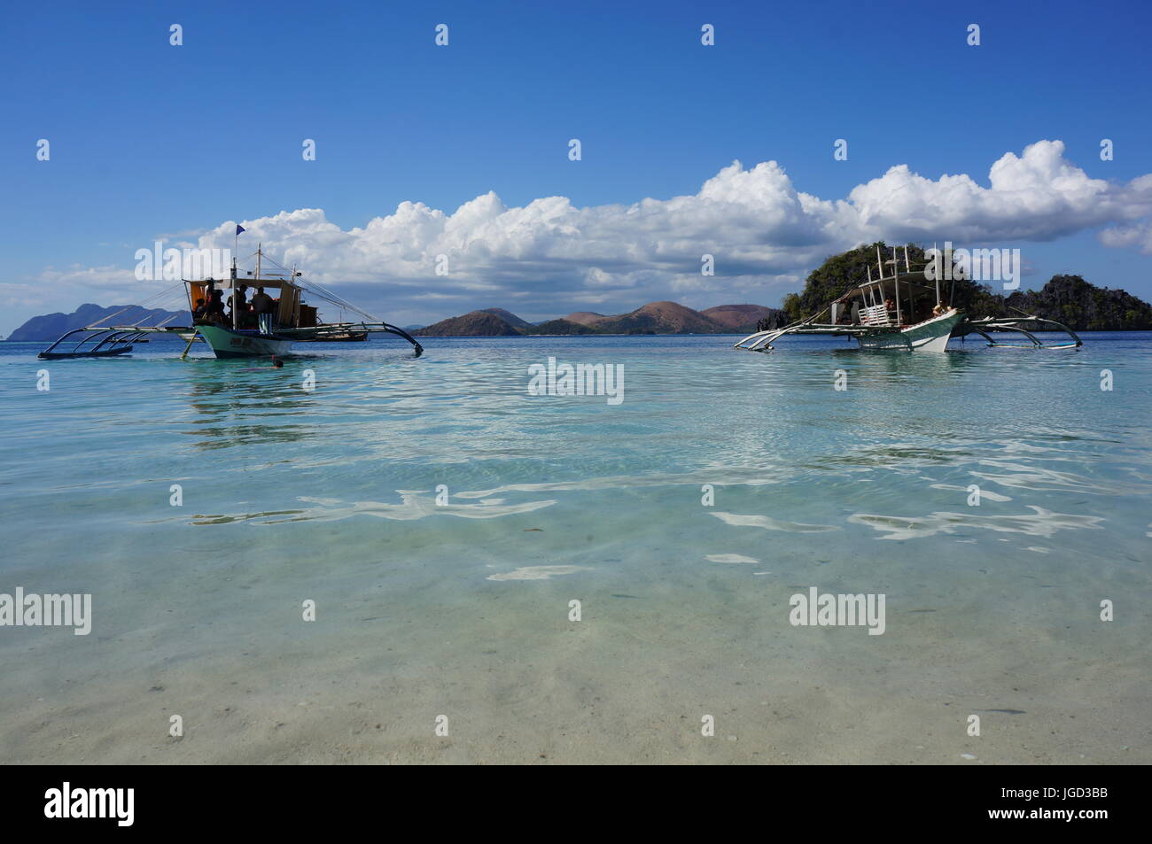 Angelboote/Fischerboote umgewandelt für Touristen.  Low shot Sand, blaues Meer, Boote, Hügel Bereich / Klippen, strahlend blauer Himmel, weiße flauschige Wolken. Coron, Philippinen. Stockfoto