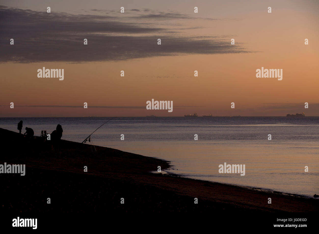 Silhouette Fischer angeln bei Sonnenuntergang an der Südküste von England. Orangefarbenen Himmel und ruhiger See auf Hayling Island. Idyllischer Weg, um einen Abend zu verbringen. Stockfoto