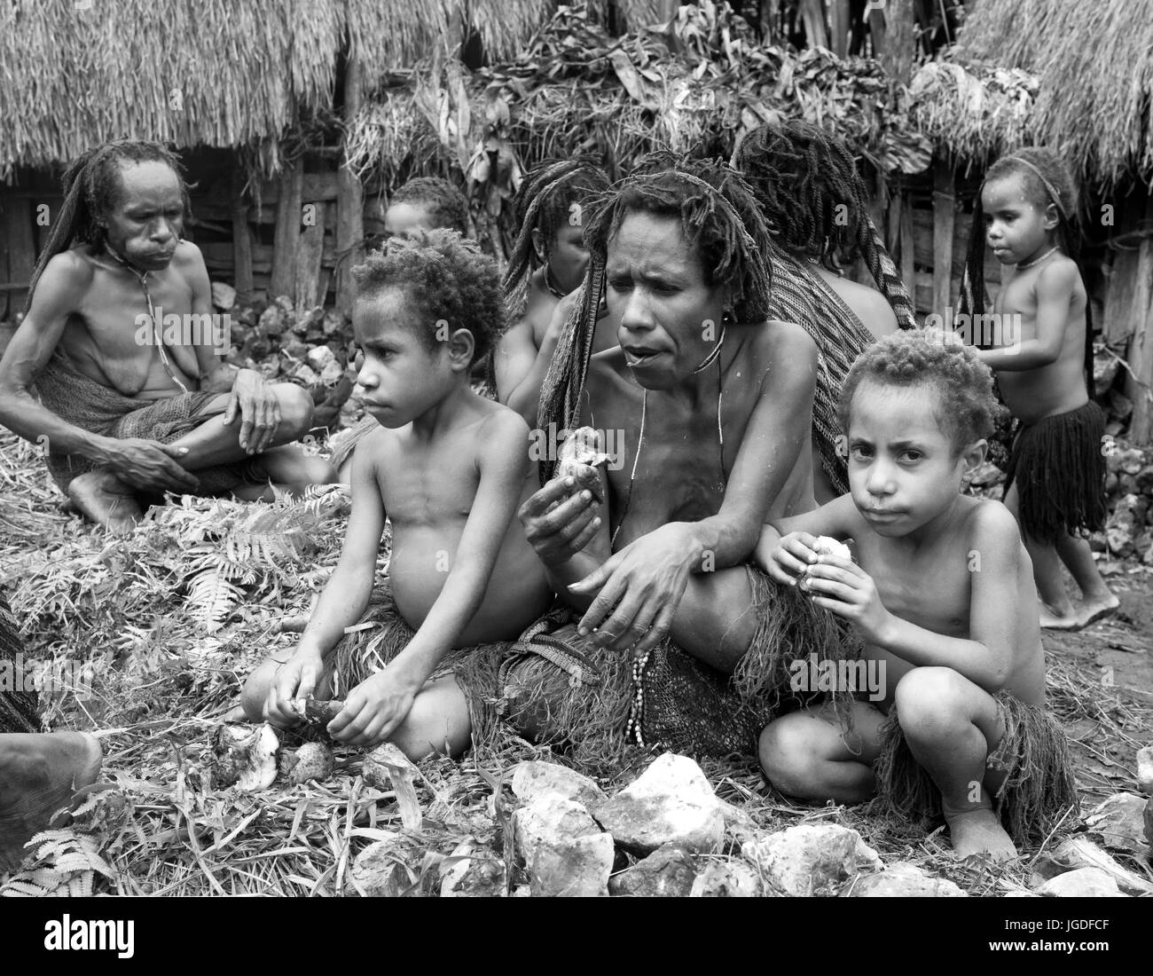 DANI-Dorf, WAMENA, IRIAN JAYA, Neuguinea, Indonesien – 25. Juli 2009: Frau mit Kindern Dani Stamm sitzen auf dem Boden im Dorf. Stockfoto