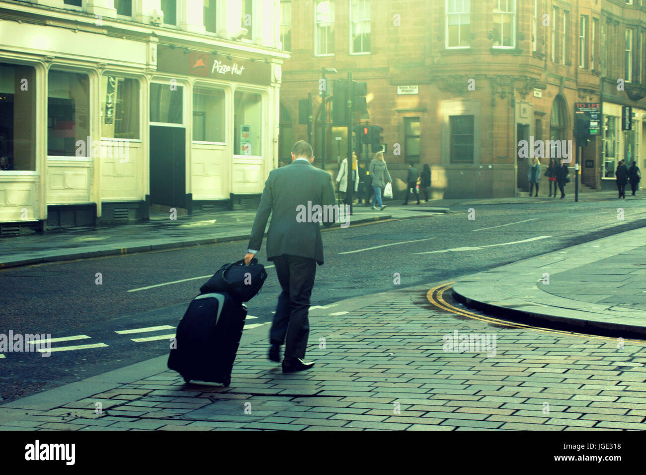 Glasgow Straße Geschäftsmann mit Gepäck zu Fuß bergauf in die helle Sonne gelb Stockfoto