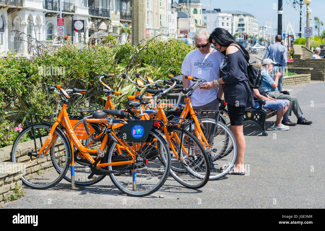 Fahrradverleih. Paar mit dem Esel Republik-app auf dem Smartphone Fahrradvermietung in Worthing, West Sussex, England, UK. Stockfoto