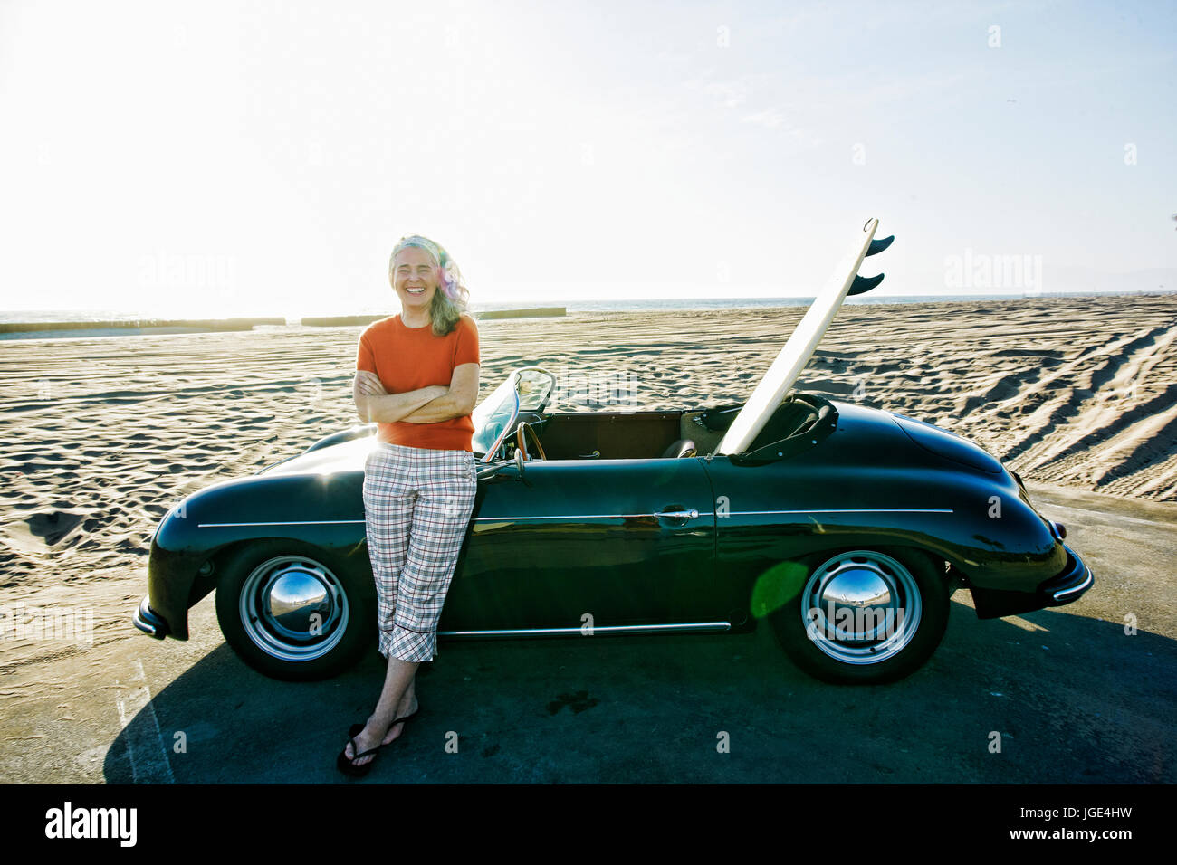 Ältere Frau kaukasischen stützte sich auf Cabrio mit Surfbrett am Strand Stockfoto