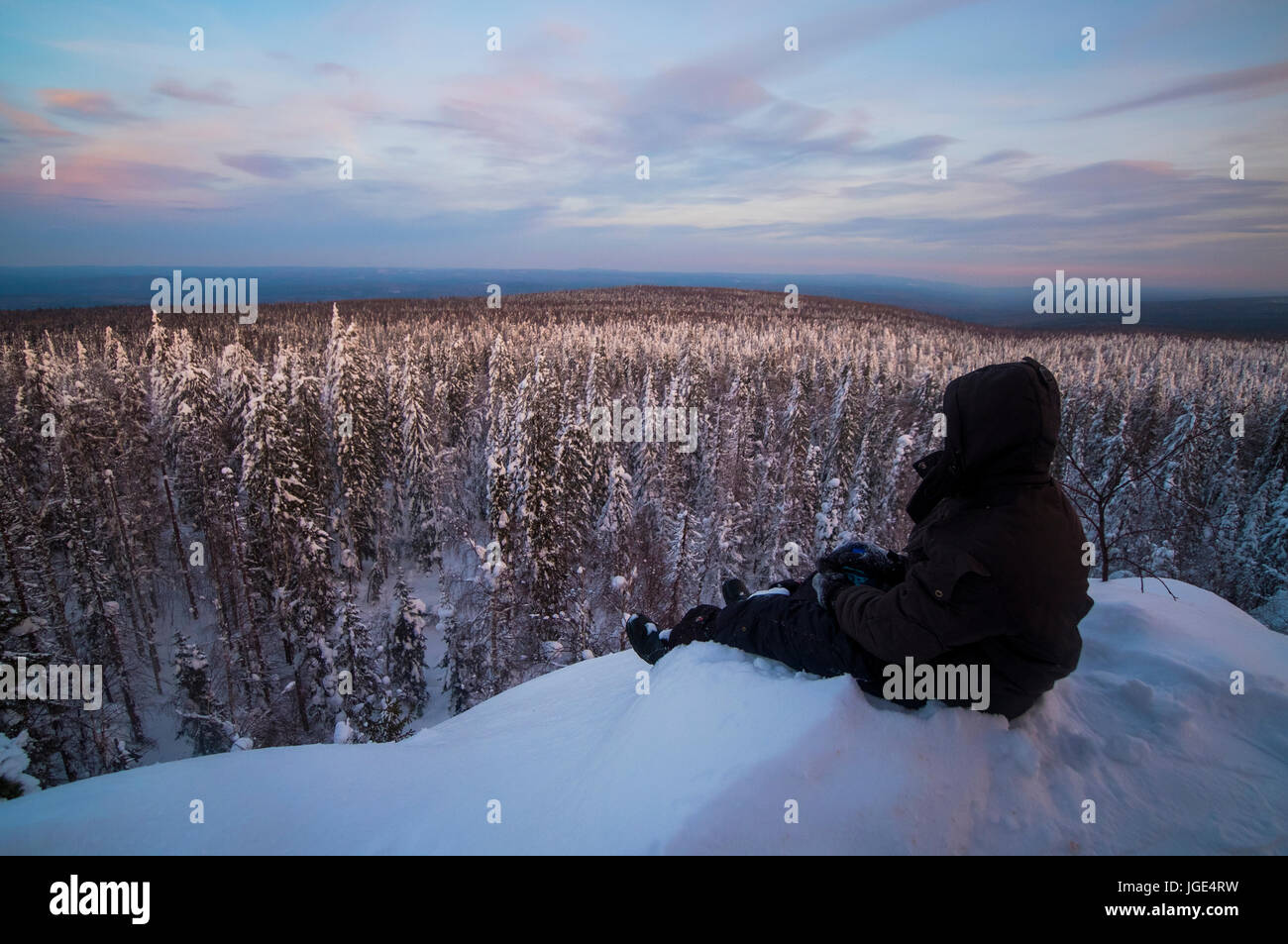 Kaukasischen Mann sitzen im Schnee, die malerische Aussicht auf Wald Stockfoto