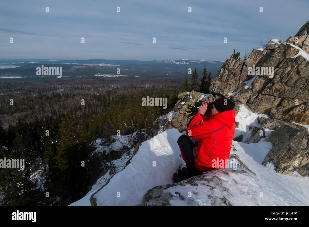 Kaukasischen Mann sitzen im Schnee, die malerische Aussicht auf Wald Stockfoto