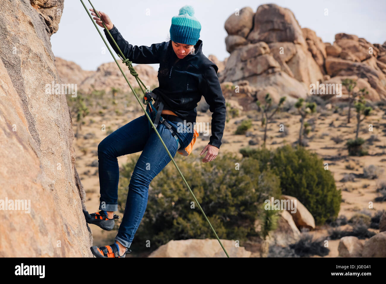 Junge Mischlinge Frau gekleidet für kaltes Wetter Felsen klettert in der Wüste Stockfoto