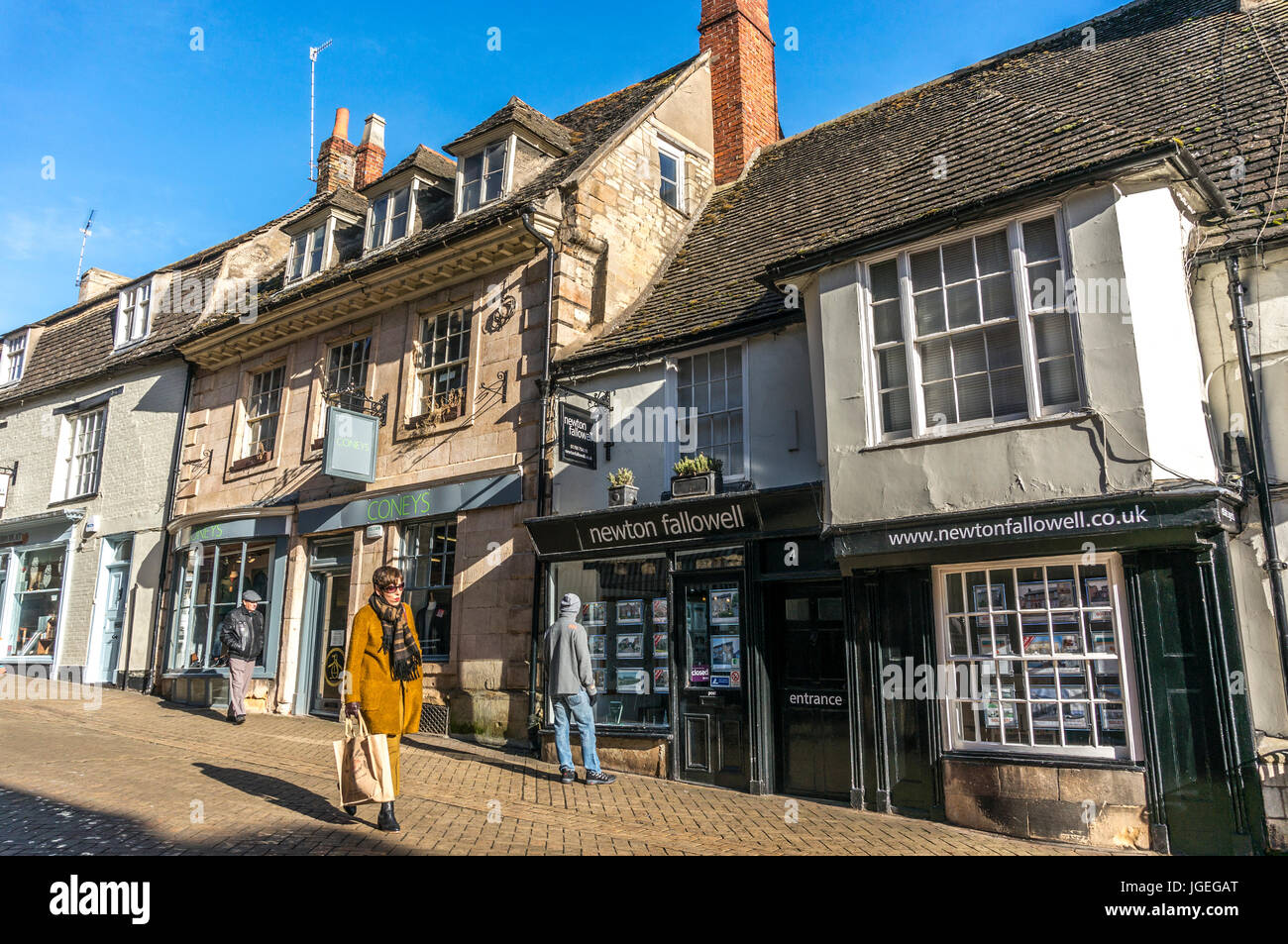 Eine gut gekleidete Frau, lokale Geschäfte und Immobilienmakler in historischen Gebäuden, früh am Morgen ein Winter in Stamford Town, Lincolnshire, England, UK. Stockfoto