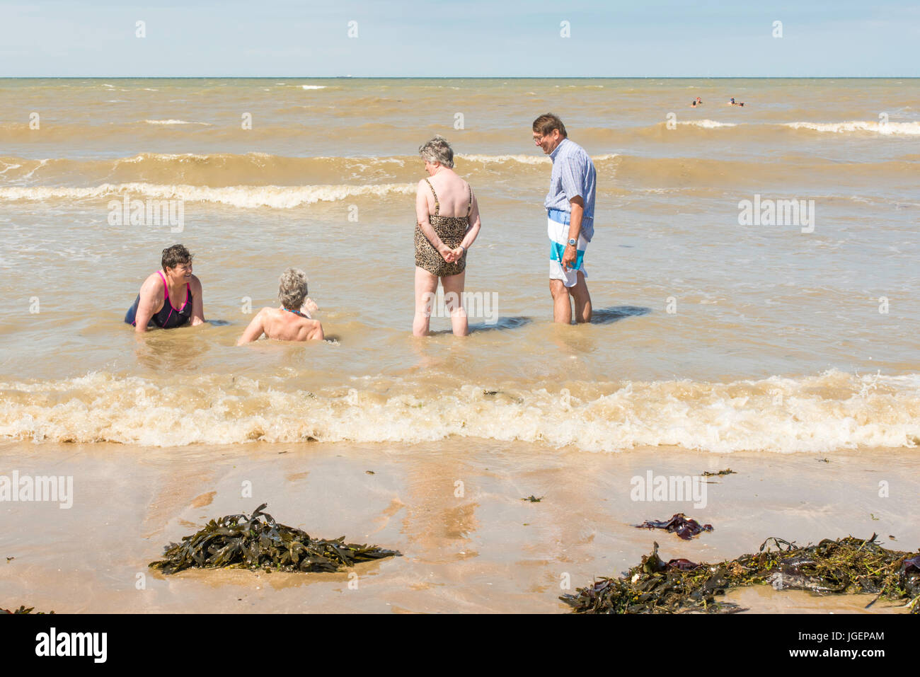 Vier ältere Menschen im Meer, am Wasser, am Strand von Westbrook Bucht, Margate, Kent an einem sonnigen Tag. Stockfoto