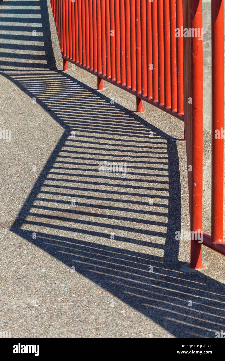 Eine abstrakte Darstellung der roten Zaun und seine Reflexion auf dem Betonboden. Stockfoto