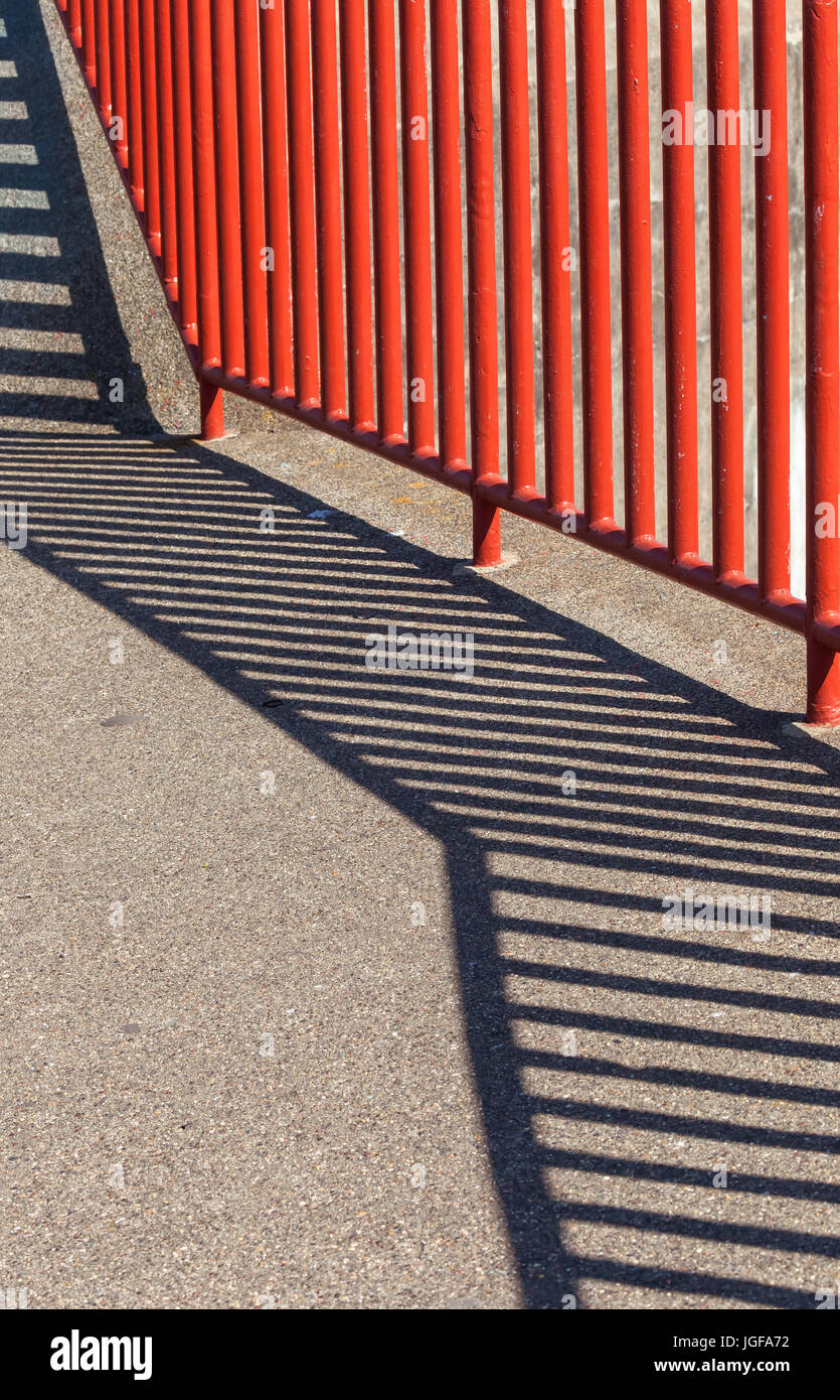 Eine abstrakte Darstellung der roten Zaun und seine Reflexion auf dem Betonboden. Stockfoto