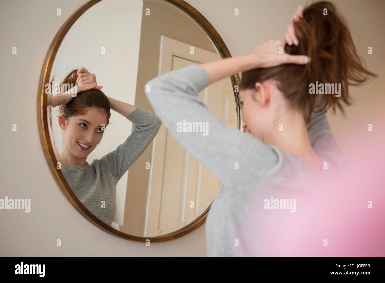 Reflexion der kaukasischen Frau im Spiegel, die Haare zurückziehen Stockfoto