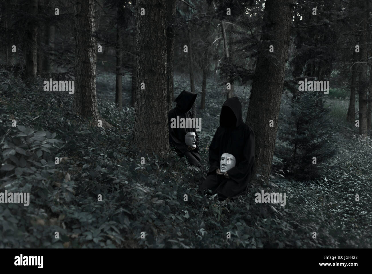 Menschen, die schwarzen Roben tragen und halten weiße Masken sitzen im Wald Stockfoto