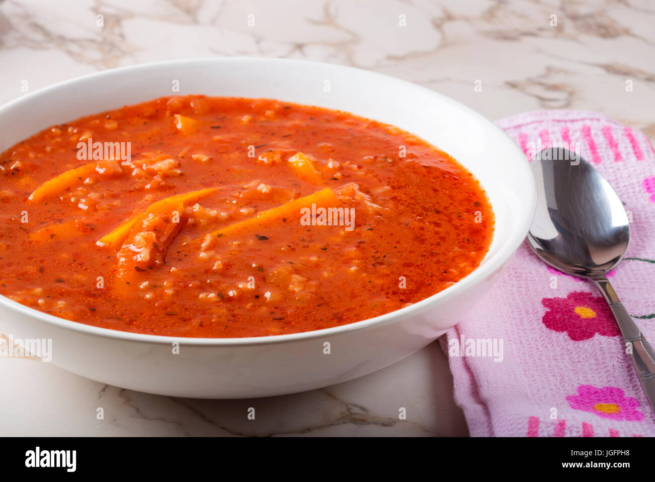 Sommer Suppe aus Tomaten-Sauce, Reis und Karotten in weißen Teller mit Löffel auf Handtuch Stockfoto