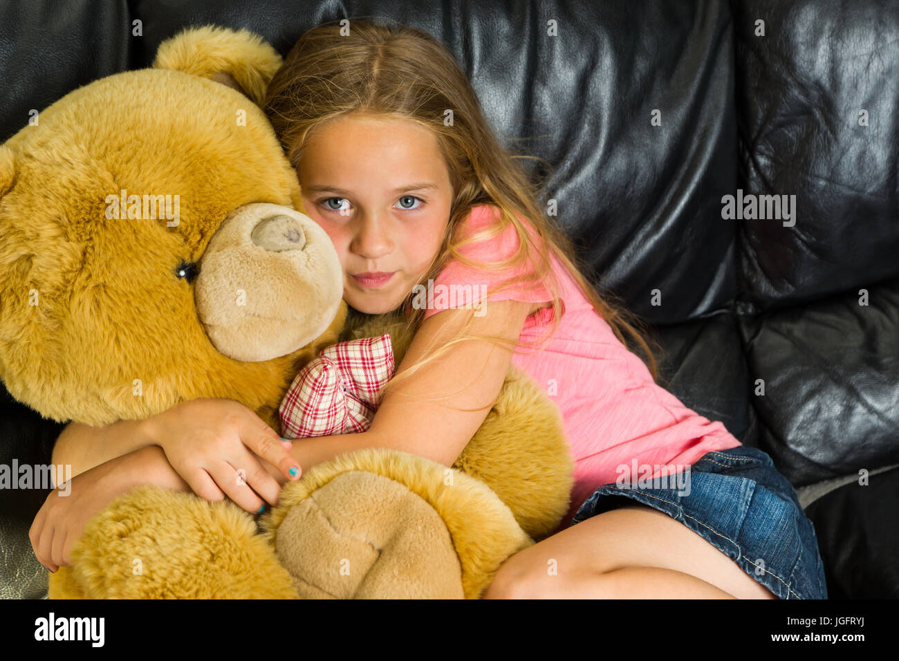 Junges blondes Mädchen umarmt Teddybär liegend auf der couch Stockfoto