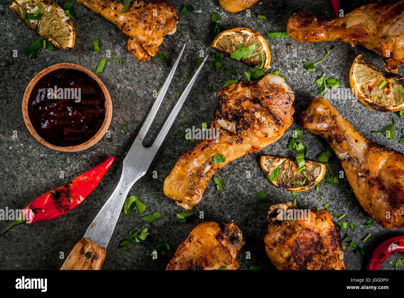 Sommer essen. Ideen für Grill, Grill-Party. Hähnchenschenkel, Flügel, gegrillt, gebraten in Brand. Mit hot Chili-Pfeffer Zitrone und Bbq-sauce. Dunkle Steintisch Stockfoto