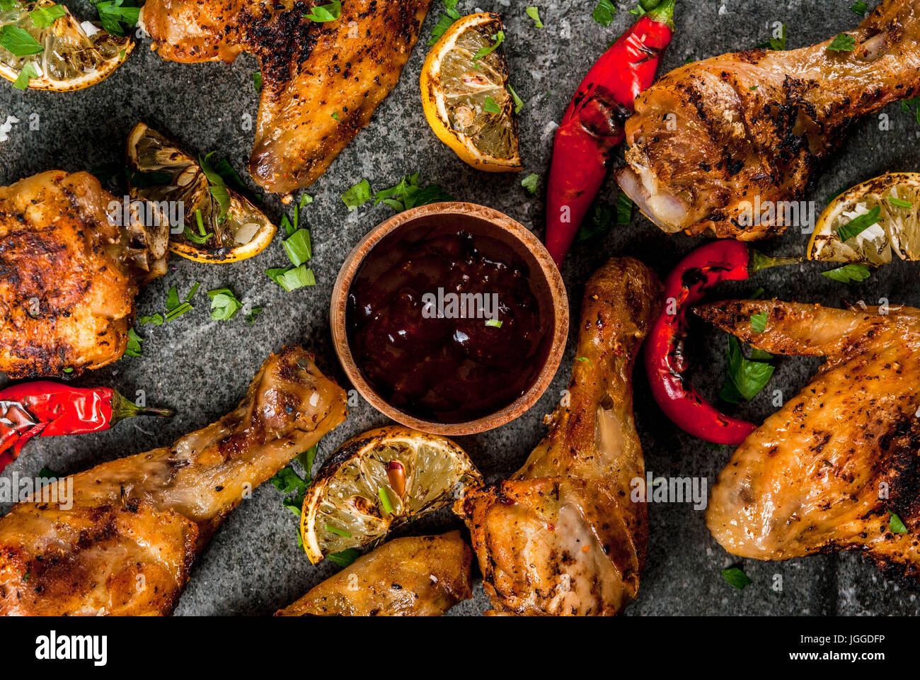 Sommer essen. Ideen für Grill, Grill-Party. Hähnchenschenkel, Flügel, gegrillt, gebraten in Brand. Mit hot Chili-Pfeffer Zitrone und Bbq-sauce. Dunkle Steintisch Stockfoto