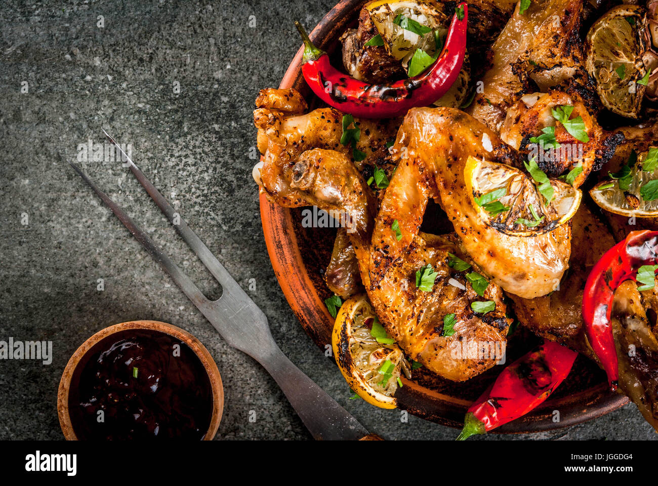Sommer essen. Ideen für Grill, Grill-Party. Hähnchenschenkel, Flügel, gegrillt, gebraten in Brand. Mit hot Chili-Pfeffer Zitrone und Bbq-sauce. Dunkle Steintisch Stockfoto