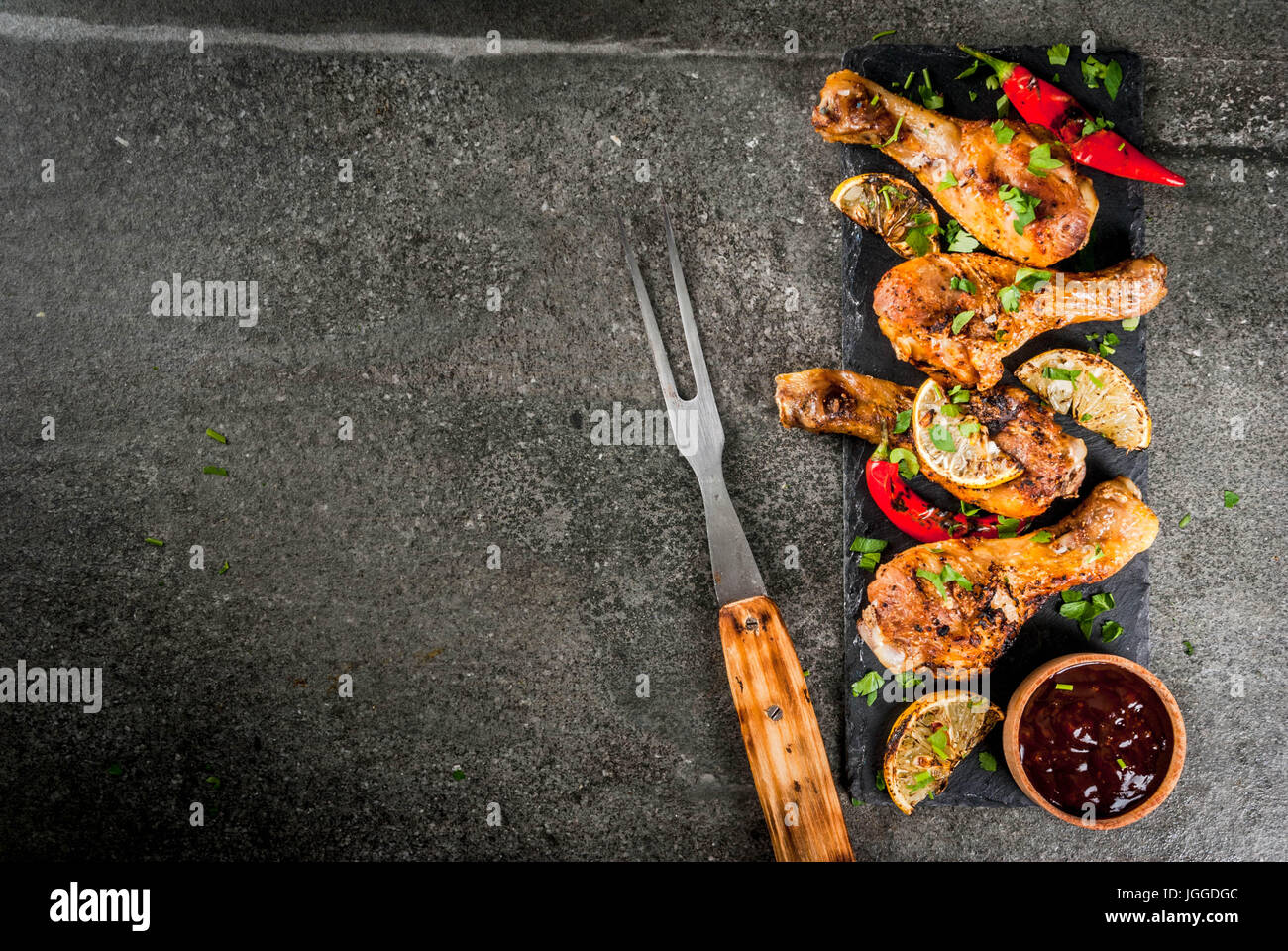 Sommer essen. Ideen für Grill, Grill-Party. Hähnchenschenkel, Flügel, gegrillt, gebraten in Brand. Mit hot Chili-Pfeffer Zitrone und Bbq-sauce. Dunkle Steintisch Stockfoto