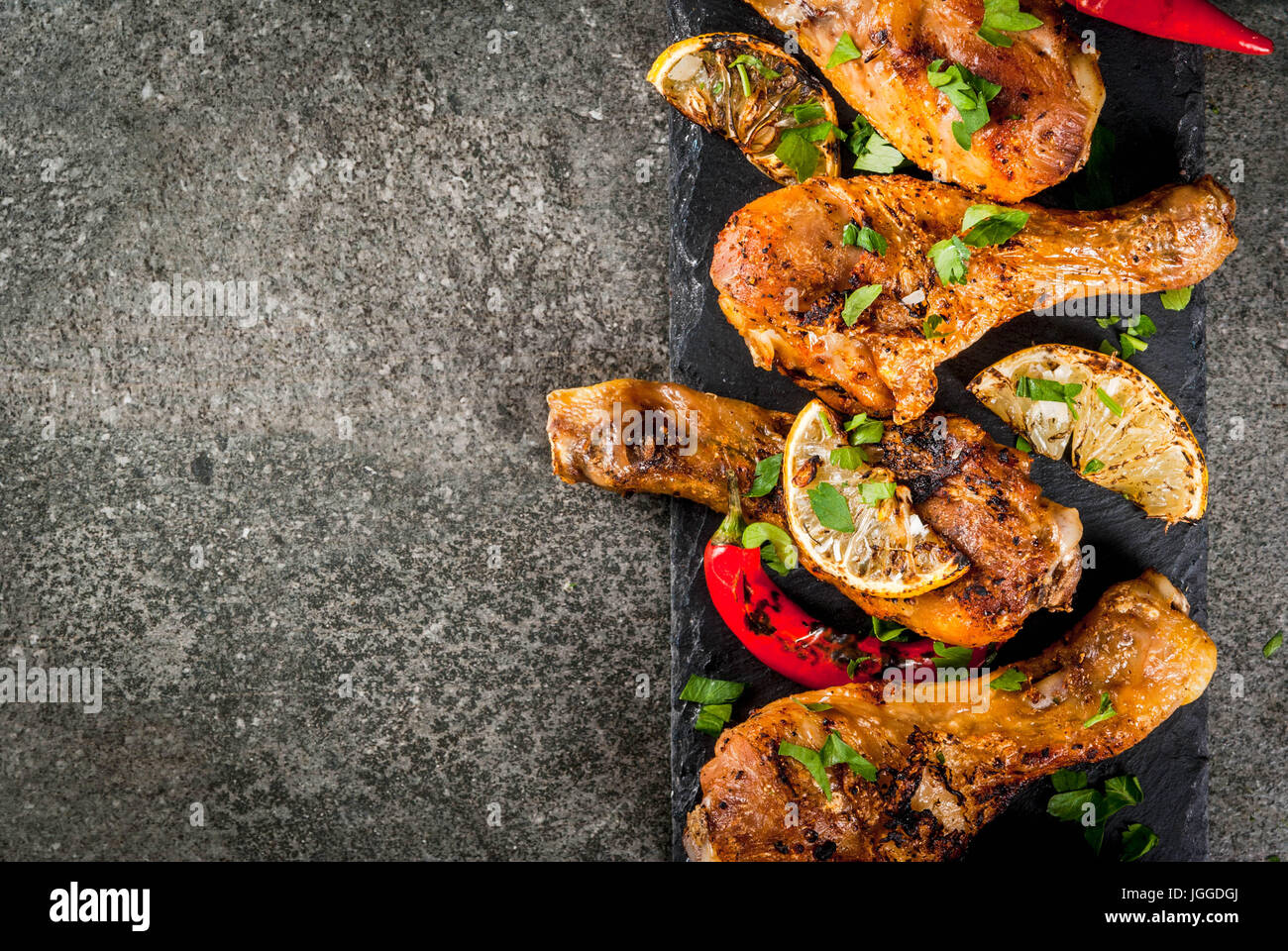 Sommer essen. Ideen für Grill, Grill-Party. Hähnchenschenkel, Flügel, gegrillt, gebraten in Brand. Mit hot Chili-Pfeffer Zitrone und Bbq-sauce. Dunkle Steintisch Stockfoto
