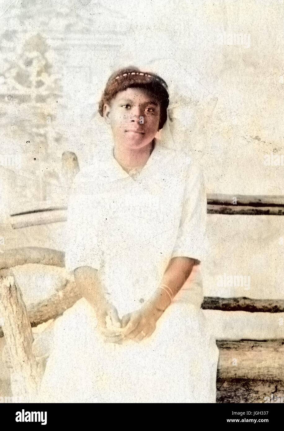 3/4 Porträt einer jungen afroamerikanische Frau, sitzt auf einer Holzbank, tragen ein weißes Kleid tragen einen Ehering mit einer ernsten Gesichtsausdruck, 1920. Hinweis: Bild wurde digital eingefärbt wurde mit einem modernen Verfahren. Farben können Zeit ungenau sein. Stockfoto