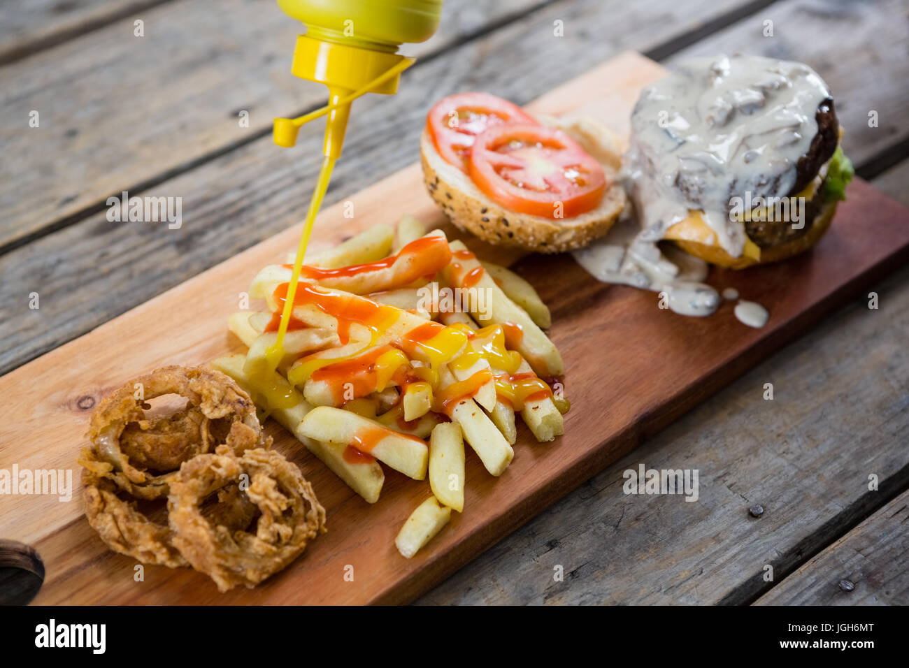 Erhöhte Ansicht der Flasche gießen Senfsauce auf Pommes frites durch Burger-Zutaten Stockfoto