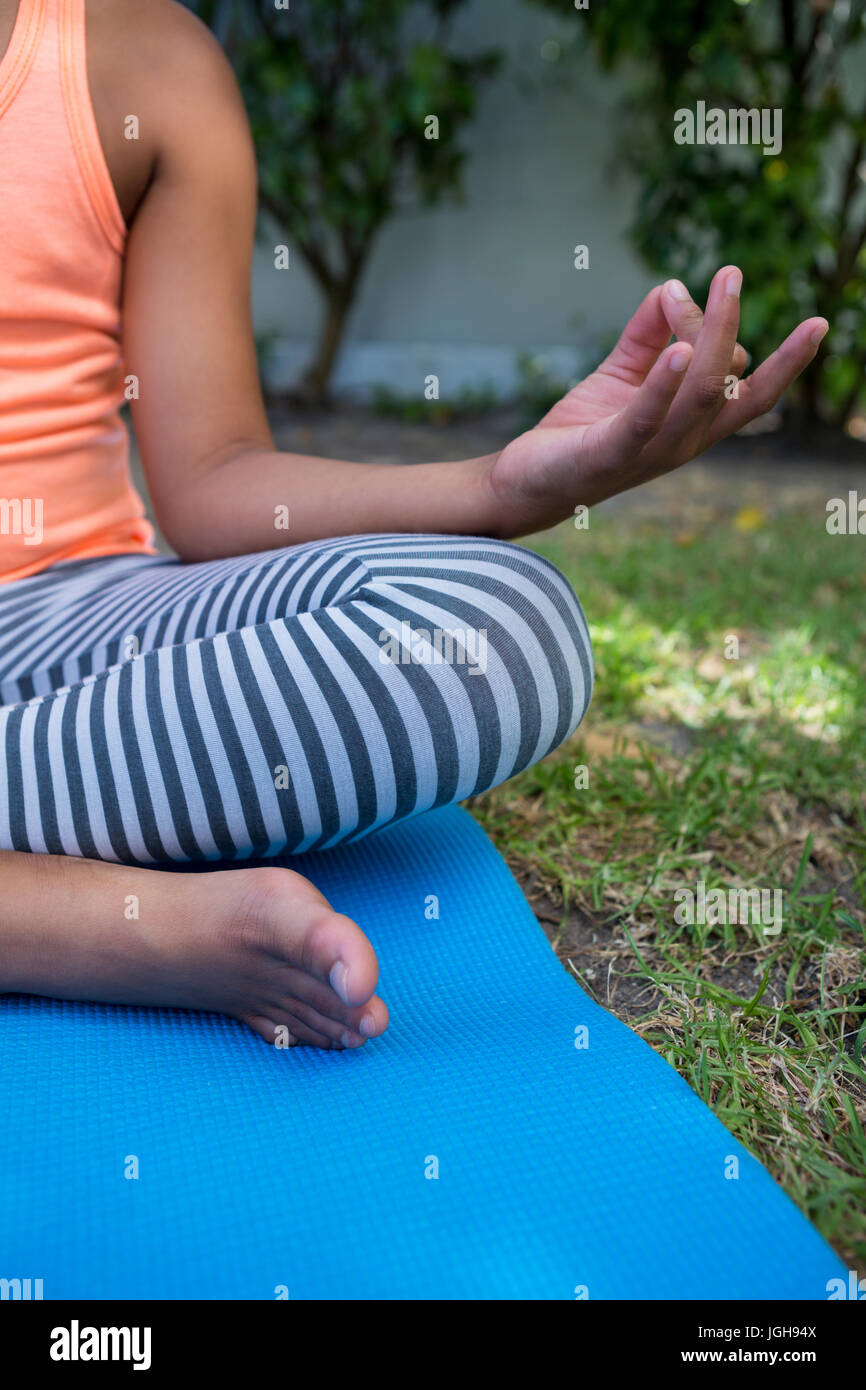 Bild des Mädchens auf Trainingsmatte im Garten sitzend meditieren beschnitten Stockfoto