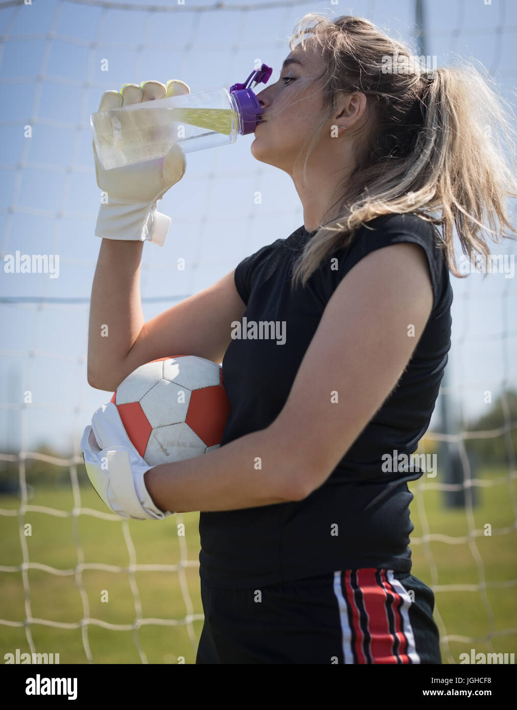 Durstig junge weibliche Fußball Spieler Trinkwasser gedrückter Kugel Stockfoto