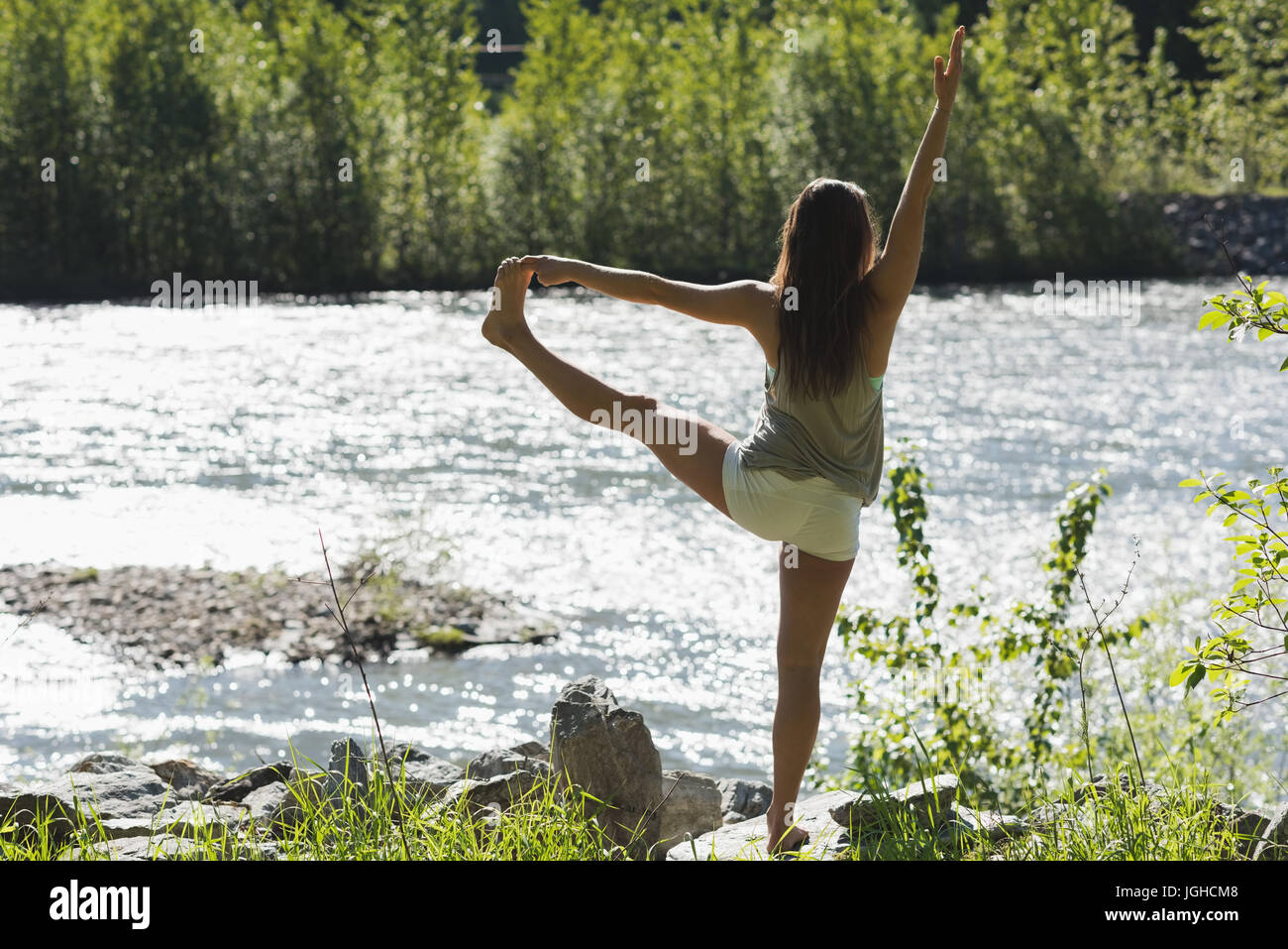 Rückansicht des Yoga in der Nähe von Riverside an einem sonnigen Tag machen Frau Stockfoto