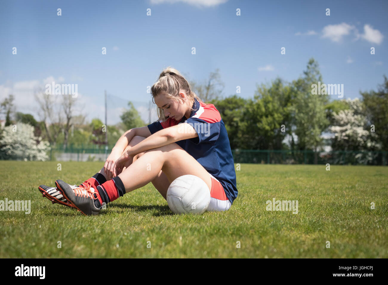 Müde Fußballspieler mit Ball sitzen auf Feld an sonnigen Tag Stockfoto
