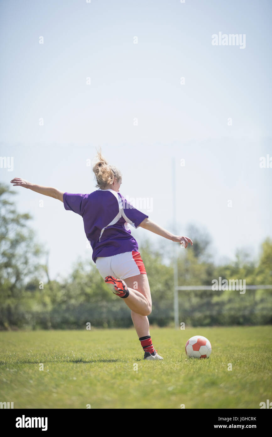 Rückansicht der Frau treten Fußball auf Feld gegen klaren Himmel Stockfoto