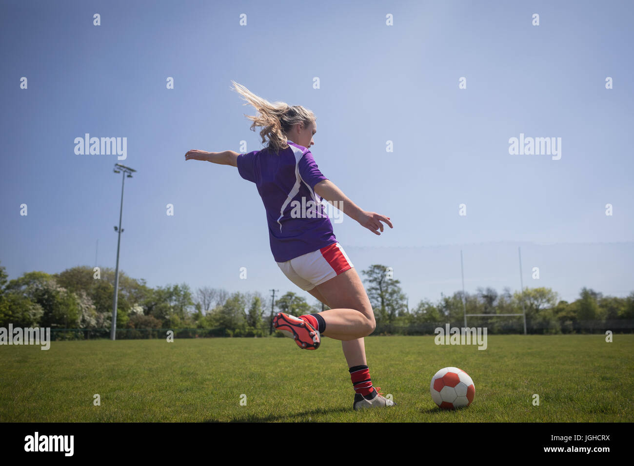 Gesamte Länge der Frau treten Fußball auf Feld gegen klaren Himmel Stockfoto