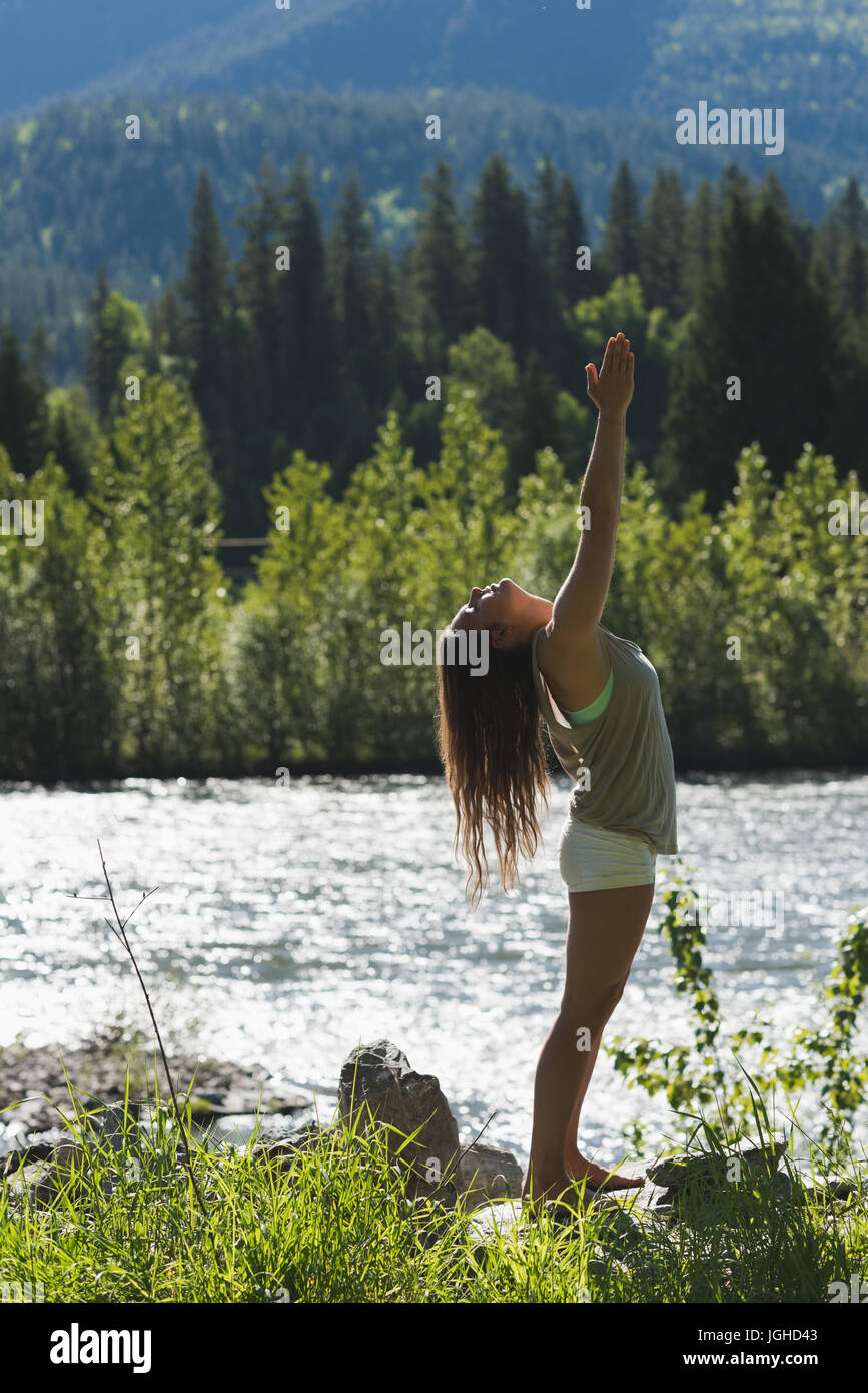 Frau, die Yoga in der Nähe von Riverside an einem sonnigen Tag machen Stockfoto