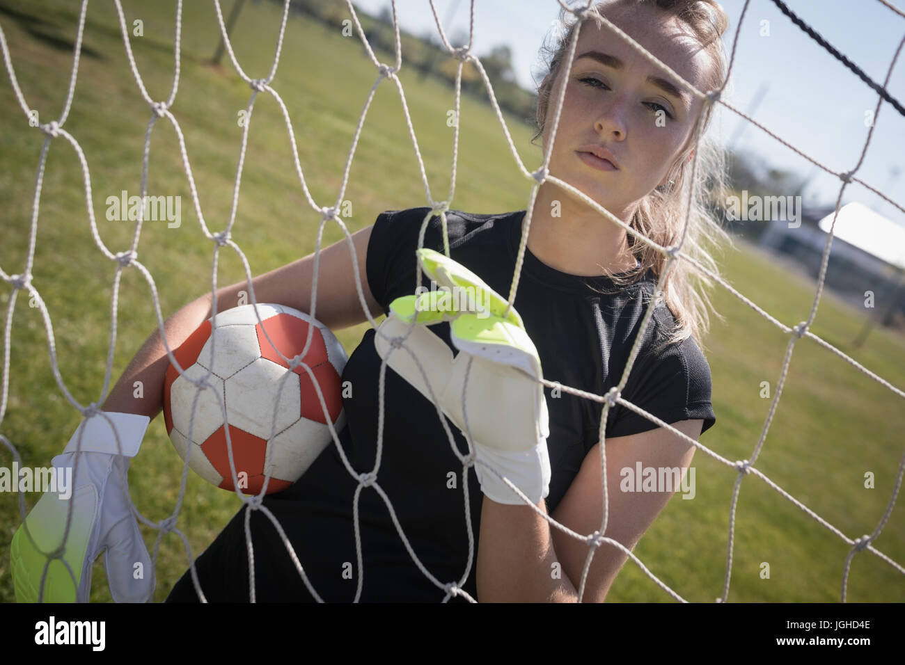 Porträt der Frau hält Fußball durch Netz auf Spielfeld Stockfoto