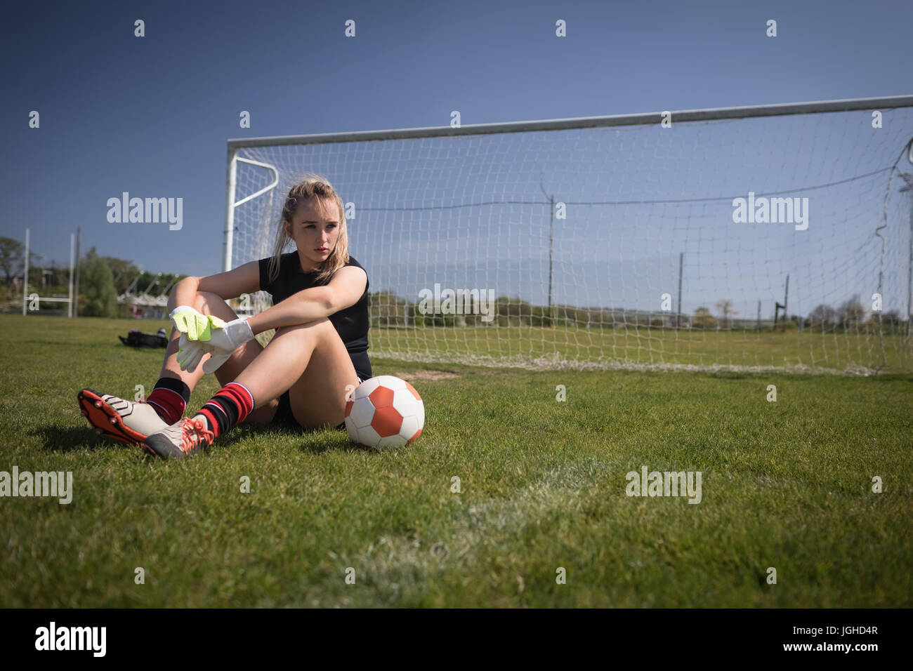 Voller Länge des weiblichen Fußballer Entspannung durch Torpfosten auf Spielfeld Stockfoto