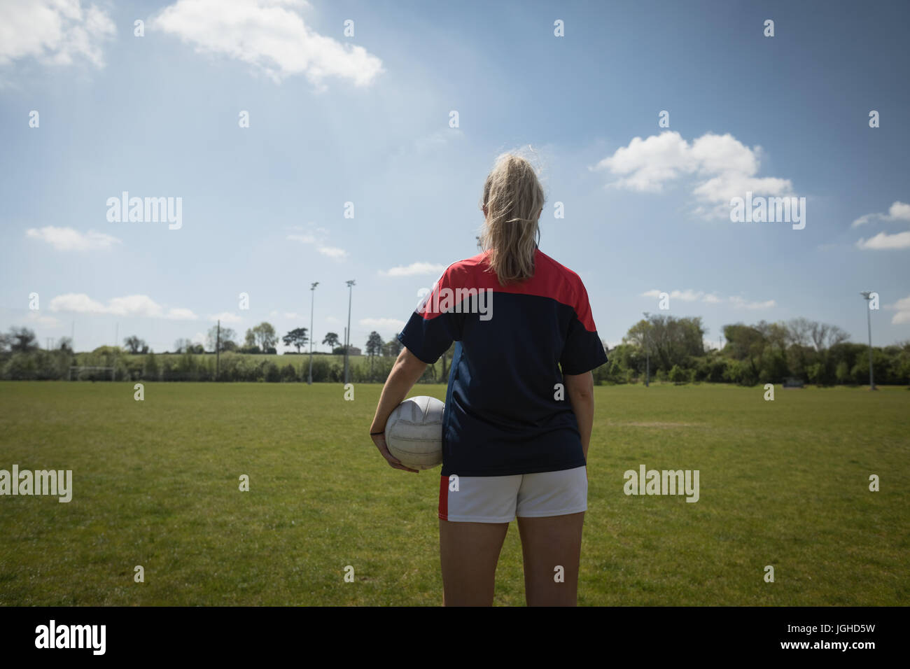 Rückansicht des weiblichen Fußballspieler mit Ball stehend auf Feld gegen Himmel Stockfoto