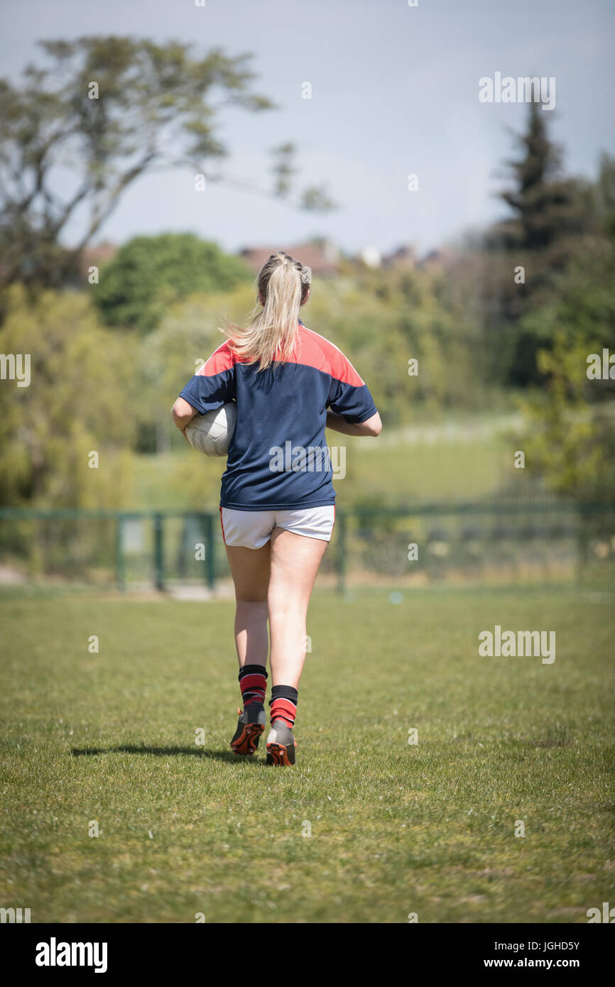 Rückseite Blick voller Länge der Spielerin läuft mit Fußball auf Feld Stockfoto