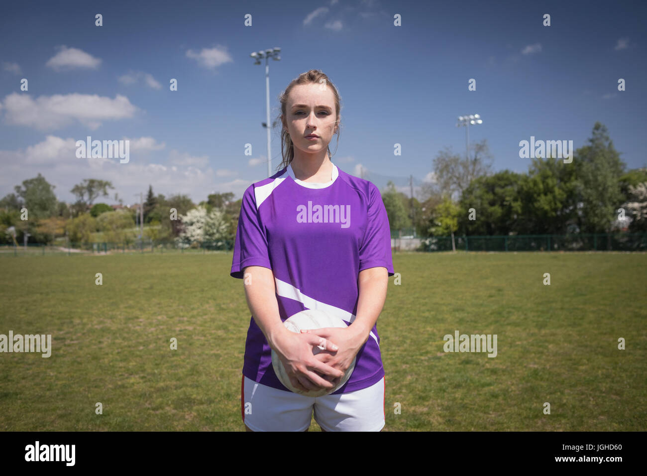 Porträt der jungen Frau, die mit Fußball auf Feld gegen Himmel Stockfoto