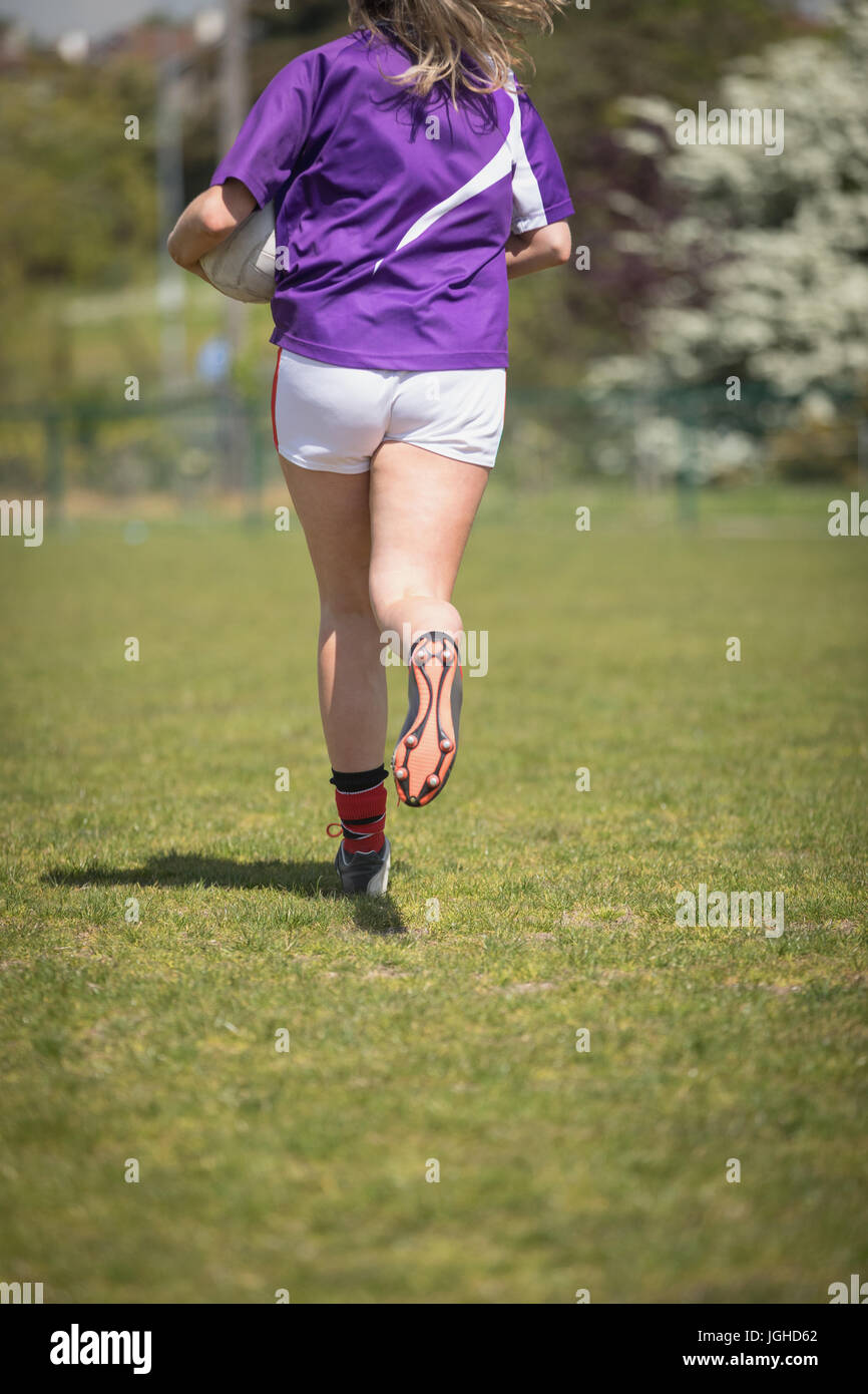 Rückansicht des Frau rennt mit Fußball auf Feld an sonnigen Tag Stockfoto