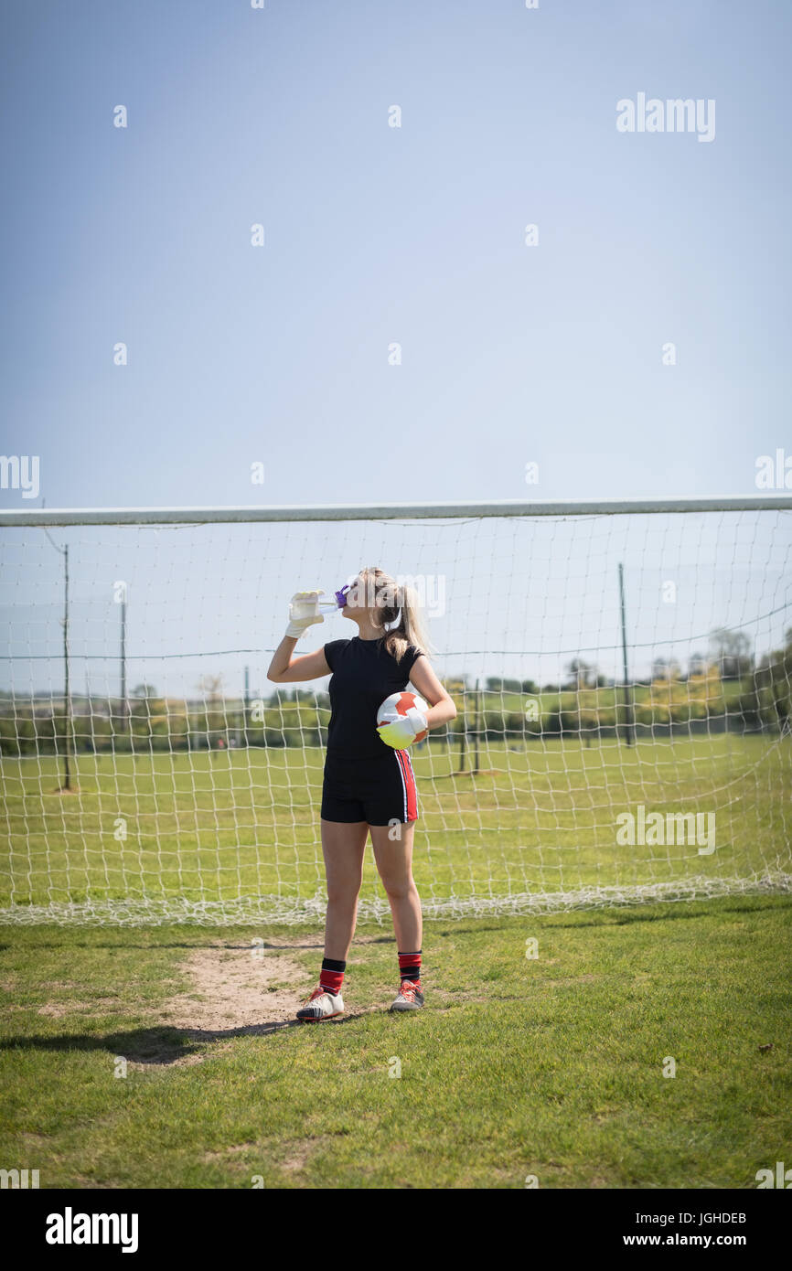 Weibliche Fußball Spieler Trinkwasser gegen Torpfosten auf Feld an sonnigen Tag Stockfoto