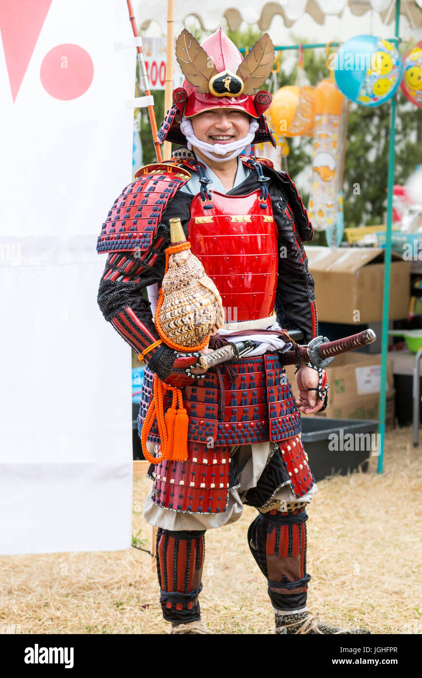 Japan, Tatsuno. April Festival. Lächelnde Menschen als Samurai Krieger in einen kompletten Anzug der roten Rüstung gekleidet, stand gegen den weißen Hintergrund für Bild posiert. Stockfoto