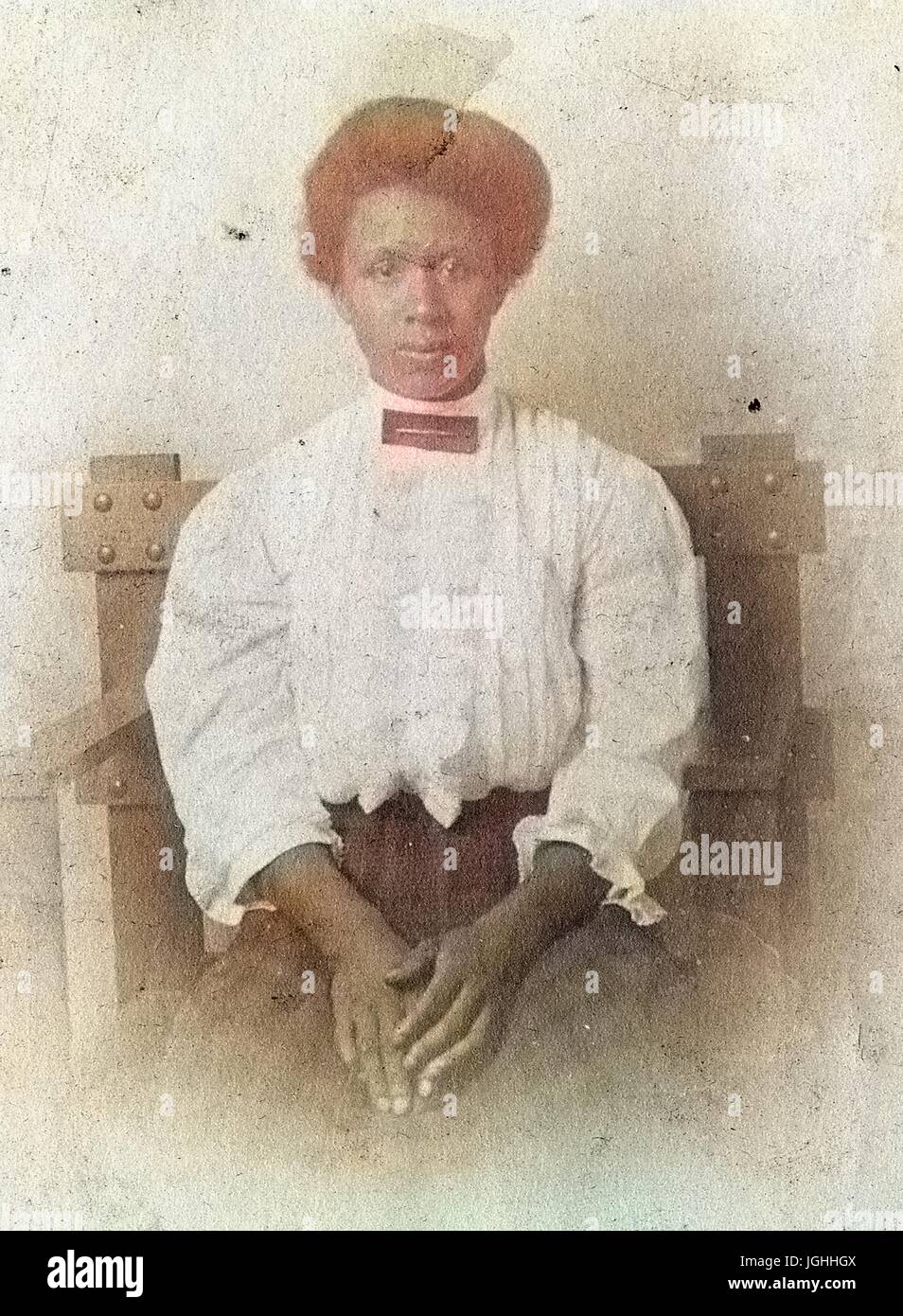 Taille bis Porträt sitzenden afroamerikanische Frau, trägt eine weiße Bluse und karierten Kleid mit einem ernsten Gesichtsausdruck Hände ruhten auf Schoß, 1920. Hinweis: Bild wurde digital eingefärbt wurde mit einem modernen Verfahren. Farben können Zeit ungenau sein. Stockfoto